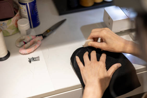 istock Woman is sewing black beanie hat on a sewing machine, using a sewing machine on the sewing table 1454350951