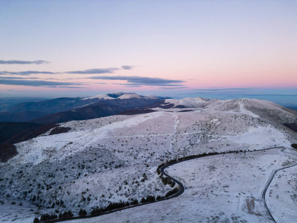 montañas cubiertas de nieve al atardecer con un camino sinuoso en primer plano vista aérea - road winding road mountain spiral staircase fotografías e imágenes de stock