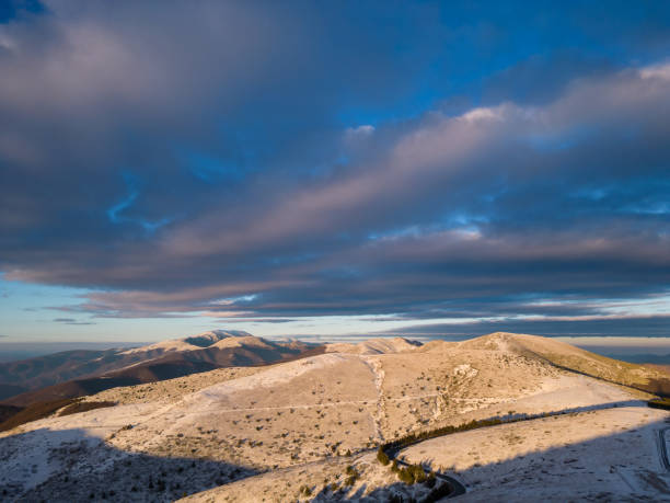 montañas cubiertas de nieve al atardecer con un camino sinuoso en primer plano vista aérea - road winding road mountain spiral staircase fotografías e imágenes de stock