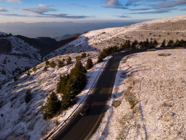 montañas cubiertas de nieve al atardecer con un camino sinuoso en primer plano vista aérea - road winding road mountain spiral staircase fotografías e imágenes de stock