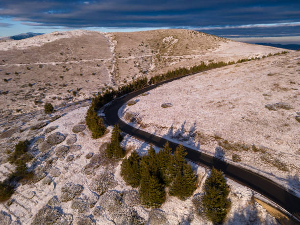 montañas cubiertas de nieve al atardecer con un camino sinuoso en primer plano vista aérea - road winding road mountain spiral staircase fotografías e imágenes de stock