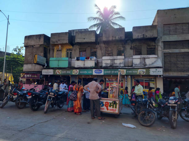 Stock photo of street food stall or panipuri chaat stall, people enjoying snacks ,two wheeler parked near the stall. residential ,commercial buildings on background. stock photo