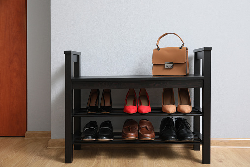 Shelving unit with shoes and stylish bag near grey wall in hallway