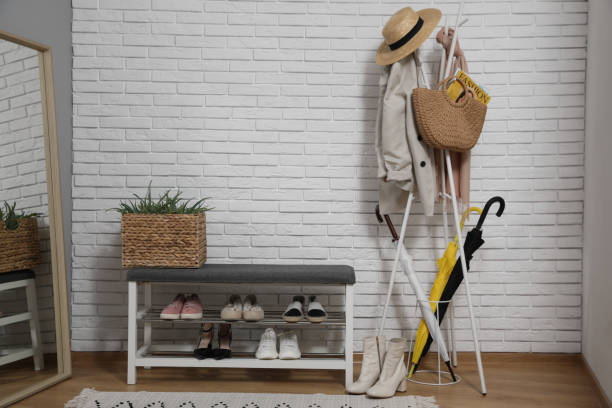 istock Stylish hallway interior with coat rack, shoe storage bench and mirror near white brick wall 1454358567
