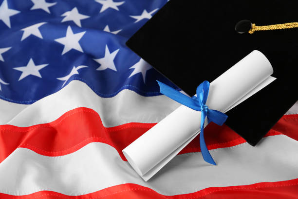 istock Black graduation hat and diploma on American flag, closeup. Space for text 1454358715