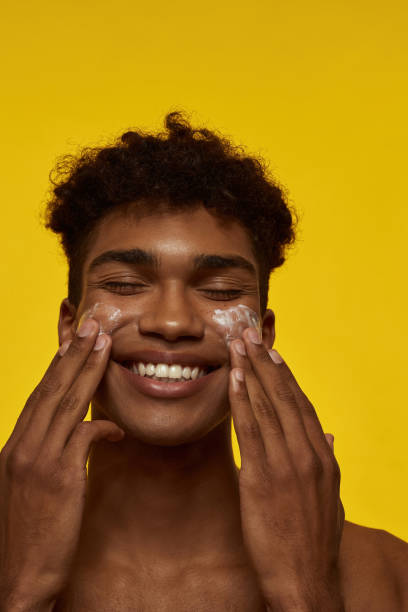 istock Smiling african guy smear cosmetic cream on face 1454359785