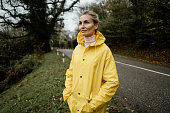 Middle aged woman in yellow raincoat walking in rainy weather in the countryside