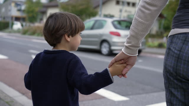 Child holding mother hands waiting to cross street at crosswalk. Family trust concept. Parent and kid hand held together