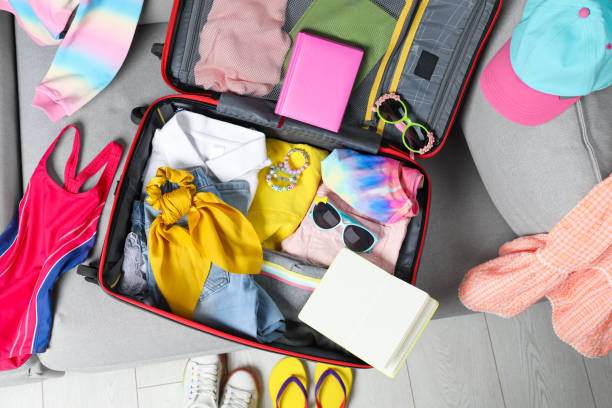 istock Open suitcase with stylish clothes and accessories on grey sofa, top view. Summer vacation 1454364424