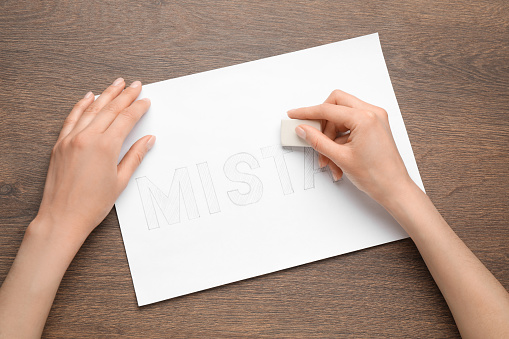 Woman erasing word on sheet of white paper at wooden table, top view