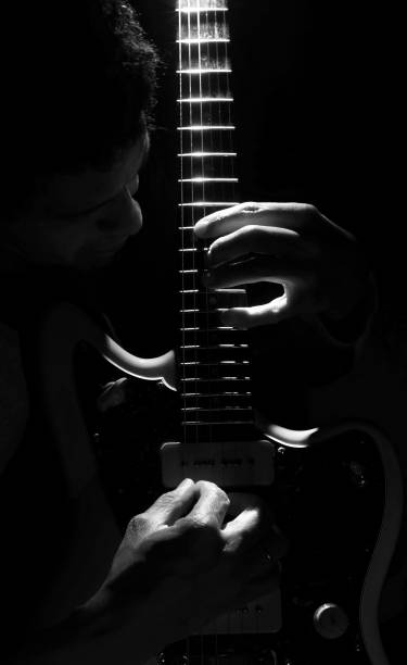istock Vertical closeup of a man playing on an electric guitar under sun rays in greyscale 1454367109