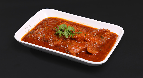 spicy red fish curry garnished with herbs served in a square bowl black background