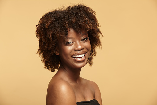 Beautiful portrait of cheerful smiling African American ethnicity woman with a clean healthy skin and afro style hairstyle standing on a beige isolated background.
