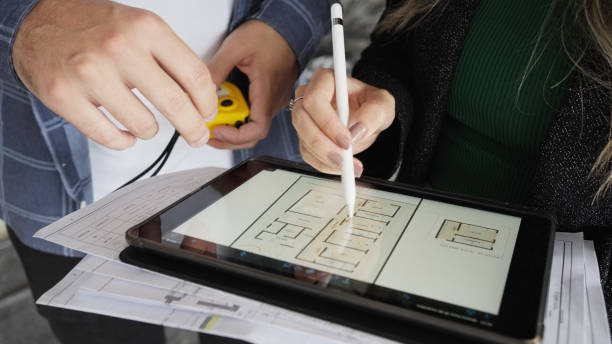 Close-up of two architects working on digital tablet at office Close-up of two architects making notes on drawing on digital tablet with blue print at office person drawing on tablet stock pictures, royalty-free photos & images