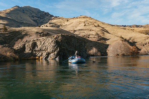 Maupin, United States – July 26, 2021: A man rowing down the river surrounded by hills in an inflatable raft
