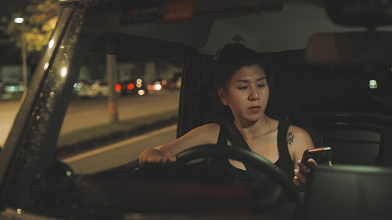 Asian Chinese woman reading phone messages at roadside stopping the car