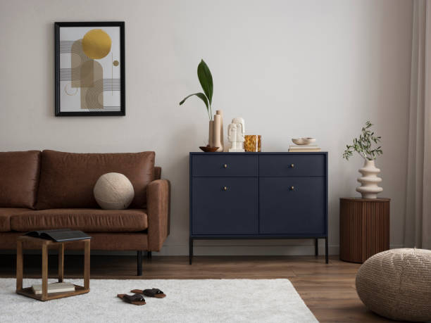 istock Interior design of harmonized living room with brown sofa, blue commode, coffee table, mock up poster frame, decoration, carpet and personal accessories. Stylish home decor. Template. 1454373122