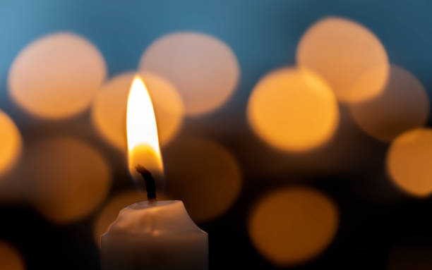istock Candle lit flame burning in yellow light in bright boekh glitter background. 1454373212