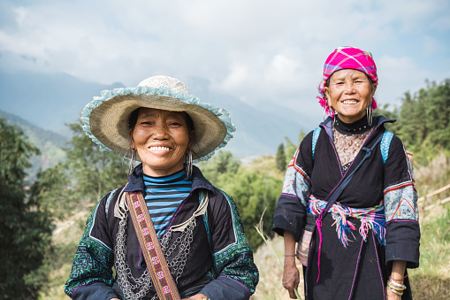portrait of two smiling indigenous woman from black hmong tribe standing in the sa pa landscape and looking to camera
