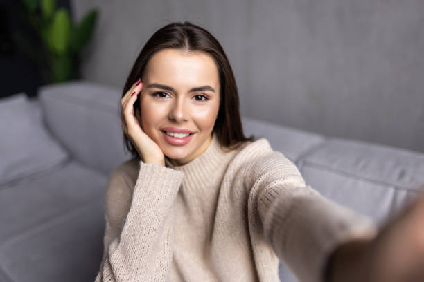 istock Cheerful beautiful woman smiling and taking selfie while resting on couch at home 1454376324