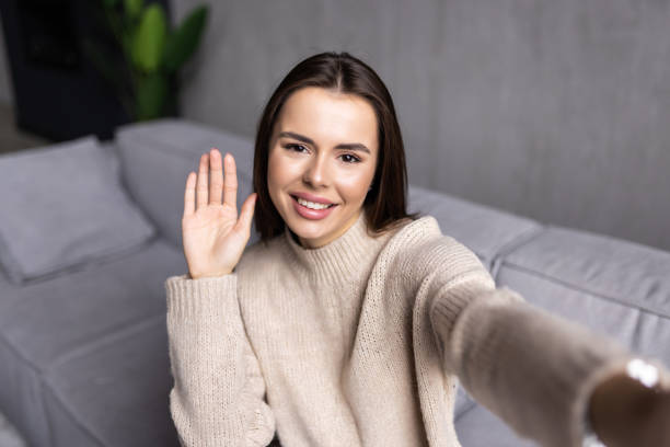 istock Cheerful beautiful woman smiling and taking selfie while resting on couch at home 1454377277