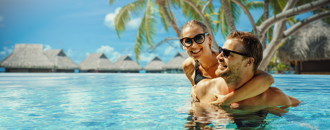 tropical resort summer vacation. happy couple relaxing in swimming pool with overwater bungalows in background.  Maldives. banner with copy space