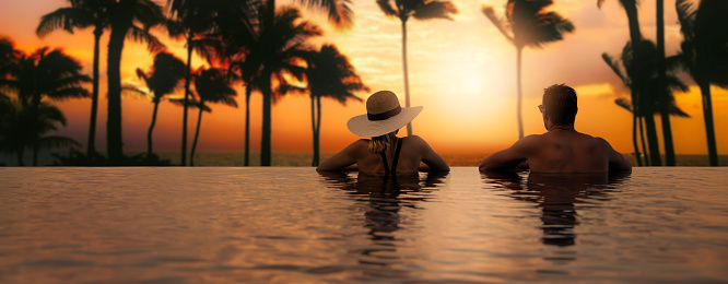 couple enjoying sunset from infinity pool at tropical Bali island resort hotel. romantic beach getaway holiday. banner with copy space