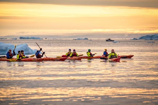 August 13, 2022 - Ilulissat, Greenland: Group of people kayaking in between icebergs at Disko Bay, north of the Artic Circle near Ilulissat Icefjord at sunset.  Ilulissat Icefjord was declared a UNESCO World Heritage Site in 2004.