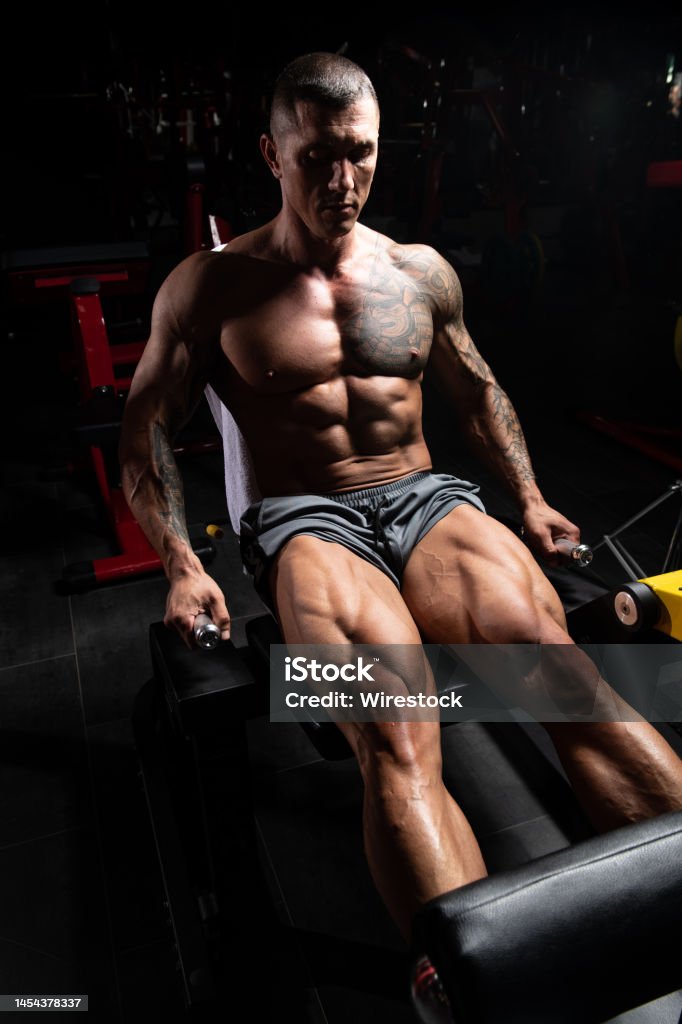 Vertical shot of a strong man in the gym, exercising quadriceps and glutes on the machine A vertical shot of a strong man in the gym, exercising quadriceps and glutes on the machine - muscular athletic bodybuilder fitness model exercise Adult Stock Photo