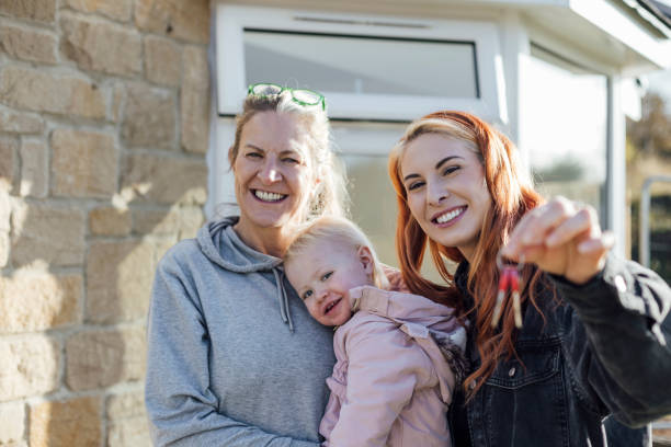 The Keys to My New Home A front-view shot of a young woman standing outside of her new home with her mother and young daughter, she is holding up her new house keys with pride. happy family with key of their new house stock pictures, royalty-free photos & images