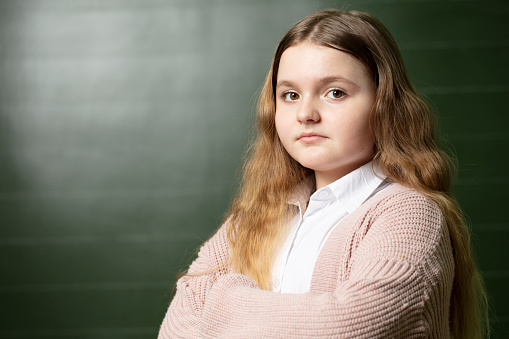 Portrait of a middle-aged schoolgirl at the blackboard. The girl stands against the background of a green blackboard and looks at the camera.