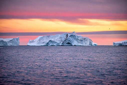 Disko Bay during midnight sun Ilulissat, Greenland. Studying of a phenomenon of global warming Ices and icebergs. Beautiful background landcape concept with multi-colored sky clouds