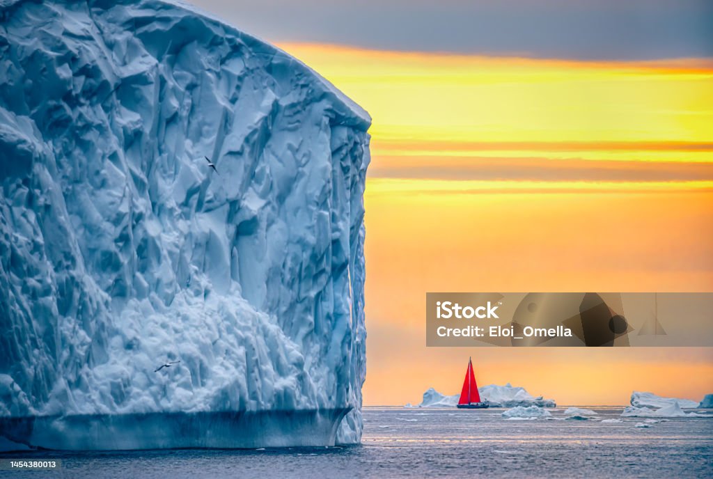 Beautiful landscape with large icebergs and red boat Arctic Icebergs on the Arctic Ocean in Greenland at sunset. Midnight sun with a red boat. Greenland Stock Photo