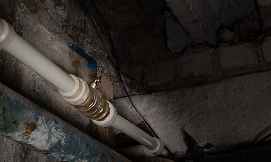 Faucet of water plastic pipe in open position on blurred background of basement wall of house with local lighting