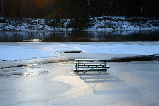 a flooded river where a bench is frozen in ice on a sunny winter day