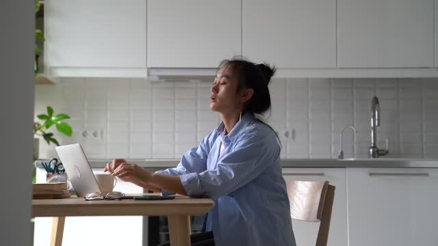Young Asian woman freelance worker stretching to reduce muscle tension while working from home