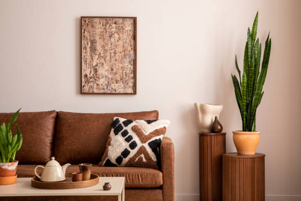 istock Creative composition of living room interior with brown sofa, mock up poster frame, beige coffee table, side table, plants and personal accessories. Stylish home decor. Template. 1454388820