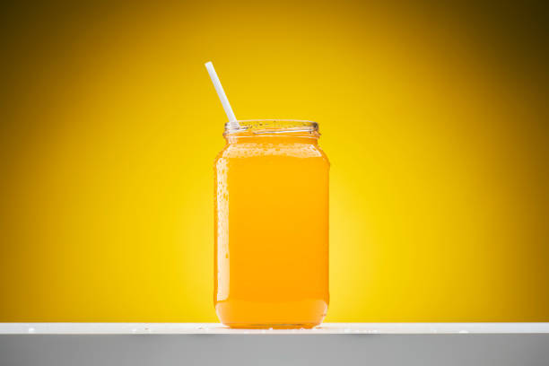 Fresh orange juice in glass jar on shelf on yellow background.
