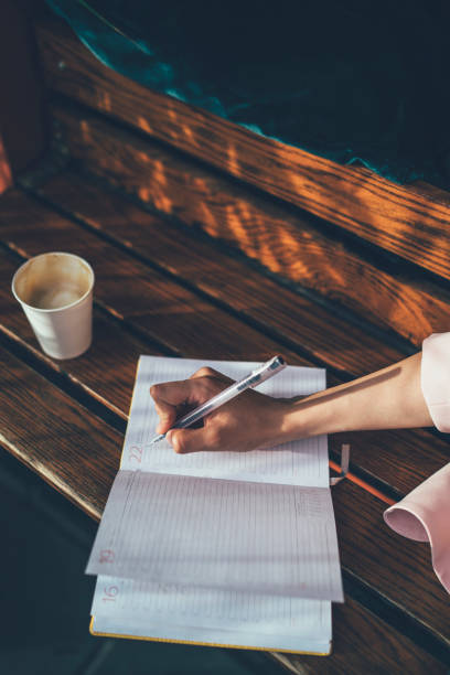istock Cropped image of intelligent female student using textbook planner for writing memo during learning process for exam preparation, selective focus on paper notepad and hand noting project information 1454396252