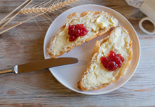 Delicious sweet breakfast plate with a fresh french croissant. Topped with butter and strawberry jam. Served on a white plate with knife on wooden table. Top view with space for text