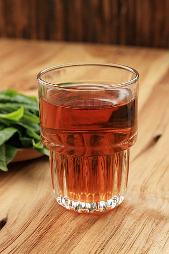 Warm Tea in A glass, with Fresh Tea Leaf Background. On Wooden Table