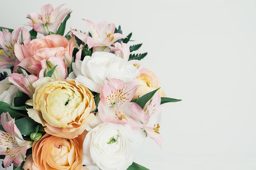 Beautiful bouquet of fresh colorful pastel ranunculus and lily flowers in full bloom with green fern leaves against white background, close up. Copy space for text.