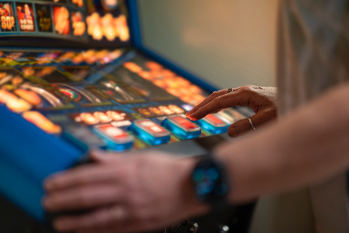 An unrecognisable woman playing a slot machine in a social club in Newcastle upon Tyne, England. She is pressing buttons on the machine and trying to win money.