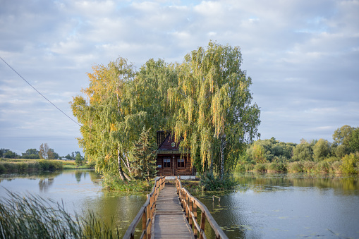 Fisherman's house with a wooden pedestrian bridge on a tiny island in the middle of the lake. Autumn view. Old Solotvyn village. Ukraine.