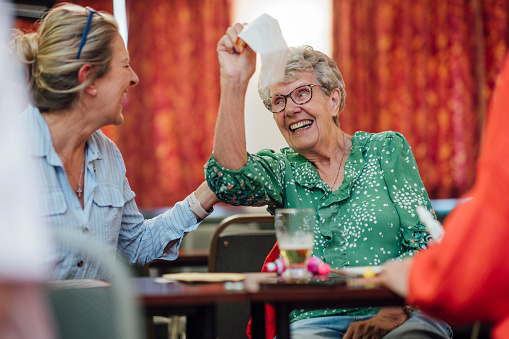 A senior woman sitting with her daughter and playing bingo in a social club in Newcastle upon Tyne, England. She is holding up her bingo card while looking at her daughter and smiling after getting the winning numbers.