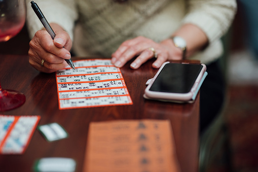 An unrecognisable woman playing bingo at a social club in Newcastle upon Tyne, England. She is marking the numbers off his sheet with a pen.
