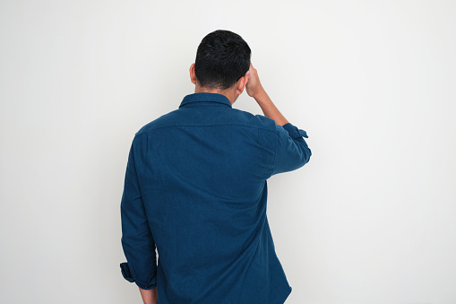 Back view of adult Asian man touching his forehead showing stress gesture