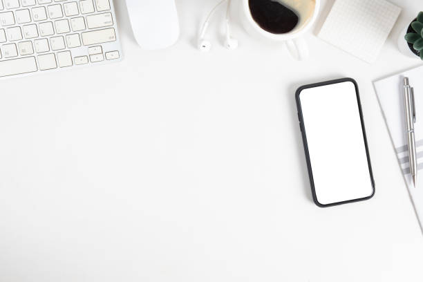 istock Mock up mobile phone with blank screen, notebook, coffee cup and keyboard on white office desk. 1454405396