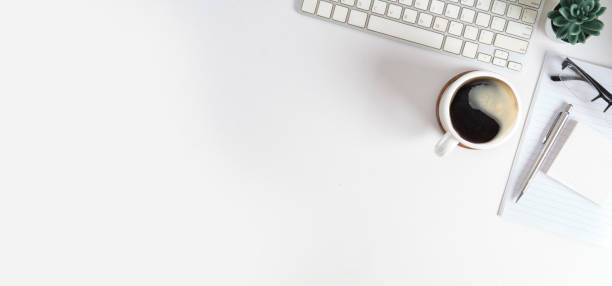 White office desk with notebook, coffee cup, keyboard and potted plant. Top view with empty copy space.