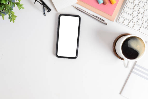 istock Top view smart phone with blank screen, coffee cup and stationery on white table. 1454406041